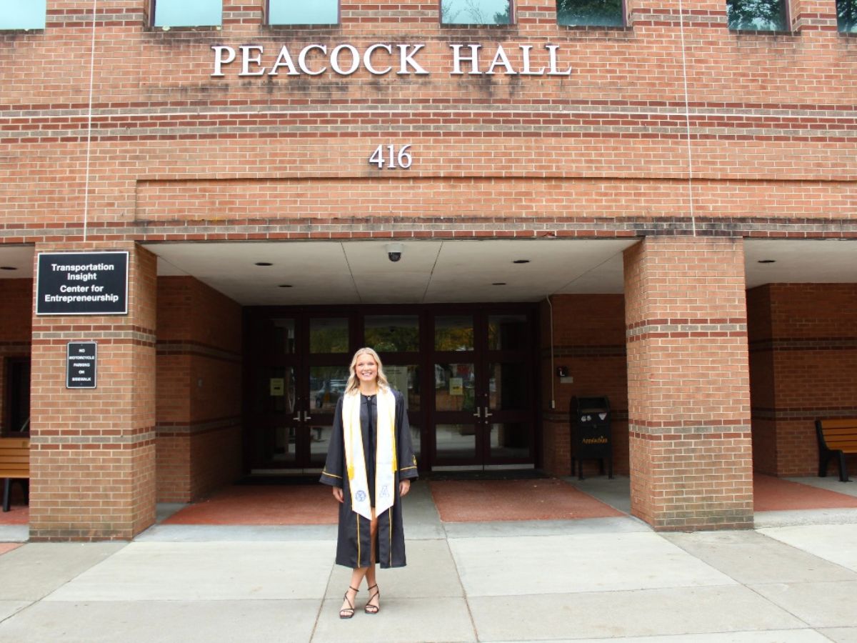 Sarah Lingle stands in graduation gown before Peacock Hall, home of the Walker College of Business.