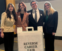 Four Presidents' Roundtable students stand with a sign with text "Reverse Career Fair" in App State's Holmes Convocation Center