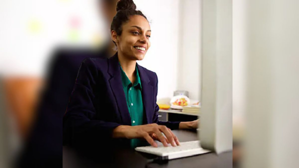 A woman, wearing a suit and smiling, types at a desktop.