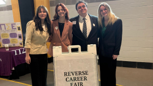 Four Presidents' Roundtable students stand with a sign with text "Reverse Career Fair" in App State's Holmes Convocation Center